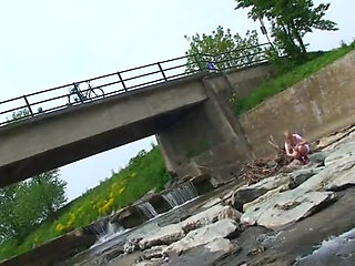 Blonde pissing outside in a river